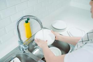 jovem com avental lavando pratos na cozinha moderna foto