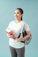 retrato de uma aluna amigável feliz com mochila segurando livros isolados sobre fundo azul foto