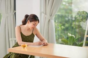 linda jovem alegre sentada à mesa da cozinha, tomando notas em um diário foto