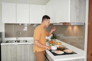 homem feliz cozinhando comida deliciosa e saudável na cozinha loft em casa em dia ensolarado foto