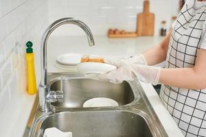 imagem recortada de mulher jovem e atraente está lavando pratos enquanto faz a limpeza em casa foto