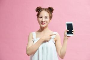 retrato de uma garota casual sorridente, apontando o dedo para o celular de tela em branco isolado sobre fundo rosa foto