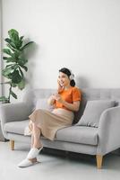menina com fones de ouvido ouvindo música no celular sentado em um sofá foto