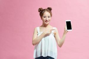 jovem feliz vestida de verão apontando o dedo para o celular de tela em branco isolado sobre fundo rosa foto