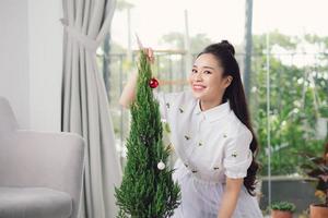 mulher jovem feliz segurando uma bola de natal na frente da árvore de natal foto