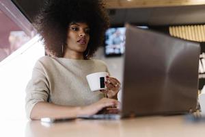 retrato de mulher afro atraente usando laptop na cafeteria