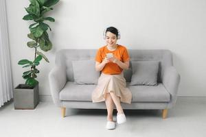 retrato de uma jovem alegre ouvindo música com telefone celular enquanto descansava em um sofá em casa