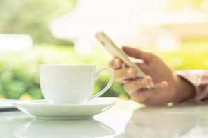 mãos masculinas segurando um telefone inteligente e uma xícara de café na mesa foto