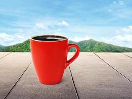 café em uma caneca vermelha colocada sobre uma mesa de madeira com montanhas e céu como um belo pano de fundo. foto