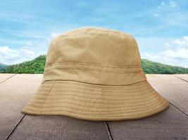 um chapéu de balde marrom é colocado sobre uma mesa de madeira contra um fundo de montanhas e céu. foto