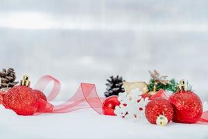 natal de inverno - bolas de natal com fita na neve, conceito de férias de inverno. bolas vermelhas de natal, bolas douradas, decorações de pinho e flocos de neve em fundo de neve foto