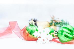 natal de inverno - bolas de natal com fita na neve, conceito de férias de inverno. bolas verdes de natal, bolas douradas, decorações de pinho e flocos de neve em fundo de neve foto
