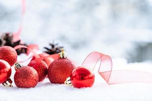 natal de inverno - bolas de natal com fita na neve, conceito de férias de inverno. bolas vermelhas de natal, bolas douradas, decorações de pinho e flocos de neve em fundo de neve foto