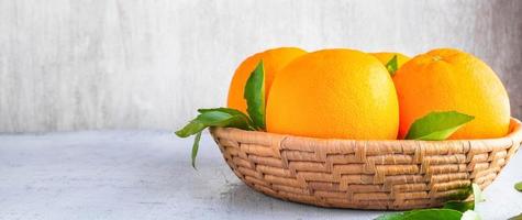 frutas frescas de laranja na cesta e folhas de laranja no fundo branco de madeira foto