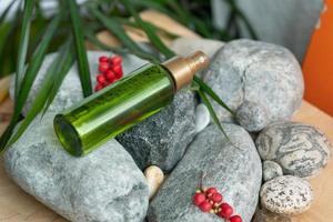 uma garrafa de cor verde com um frasco de spray está nas pedras, ao lado das folhas verdes e bagas de schisandra chinensis foto