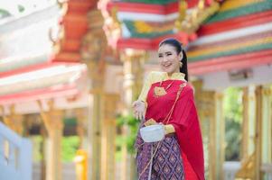 uma bela mulher tailandesa de vestido tailandês com ornamentos de ouro segura um copo de água para o festival songkran ou ano novo tailandês foto
