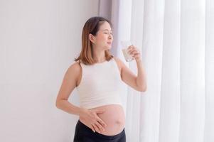 jovem mulher asiática em pé no quarto segurando um copo de leite fresco foto