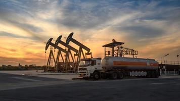 plataformas de petróleo e caminhões de petróleo estão trabalhando ou estacionados para drenar petróleo em campos de petróleo. ao pôr do sol ou nascer do sol à noite ou de manhã