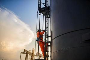 homem que trabalha em plataforma de petróleo ou campo de petróleo, escala o tanque de óleo para trabalhar à noite com surpresa ou pôr do sol. foto