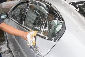 mão segure a esponja sobre o carro para lavar foto