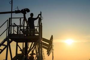 silhueta de trabalhadores de petróleo trabalhando em plataformas de petróleo ou campos de petróleo e posto de gasolina à noite com belo pôr do sol. foto
