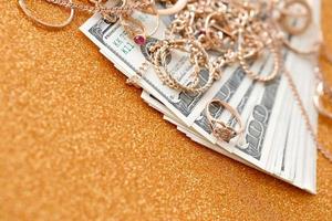 muitos anéis, brincos e colares caros de joias douradas com grande quantidade de notas de dólar na superfície de fundo dourado de brilho de luxo. loja de penhores ou joalheria foto