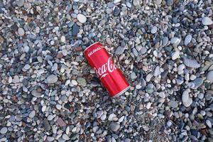 antalya, turquia - 18 de maio de 2021 lata vermelha original da coca cola encontra-se em pequenas pedras redondas perto da costa do mar. coca-cola na praia turca foto