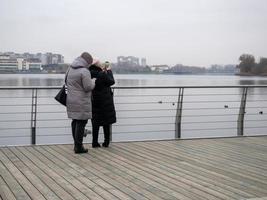 mulheres tiram fotos do lago com patos em seus telefones. nublado, dia de outono na rússia.