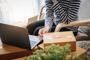 ideia de negócio de merchandising on-line, linda garota segurando uma caixa de entrega de encomendas e usando um computador para rastrear e rastrear números de encomendas para os clientes. foto