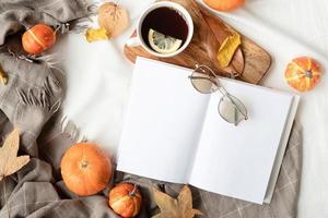 livro branco em branco com folhas de outono e xícara de chá quente na mesa, design de maquete de livro foto
