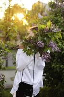 irreal deslumbrante mulher jovem e bonita andando em um verde florido na primavera em um jardim de lavanda com um buquê de lilás nas mãos. closeup retrato romântico de moda. cheirando as flores foto