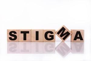 palavra estigma, texto, escrito em cubos de madeira, blocos de construção, sobre fundo branco com reflexão. foto