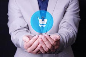 um homem, um empresário tem um logotipo de cesta de compras nas palmas das mãos. ícone de carrinho de supermercado na tela virtual. loja de varejo on-line de comércio varejista. foto