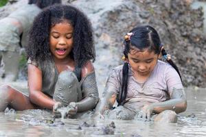 crianças se divertindo brincando na lama nos campos em um dia nublado. crianças asiáticas atravessam água e lama suja. brincadeiras ao ar livre das crianças e aprendizado fora da sala de aula foto