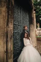 casal de noivos abraça perto da porta verde vintage. paredes de pedra no fundo da cidade antiga. noiva com cabelo comprido em vestido de renda e noivo de terno e gravata borboleta. abraço terno. Amor romântico. foto