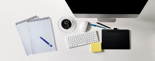 mesa branca moderna com computador de tela preta, xícara de café, caderno para escrever mensagens, canetas, vista superior foto