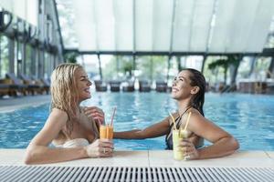 mulheres amigas bebem, coquetel mojito no bar da piscina, usam biquíni hotel de luxo perto da praia na ilha tropical relaxar. mulheres bonitas se divertindo na piscina, bebendo coquetel, sorrindo. foto