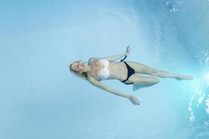 mulher jovem e atraente flutuando em uma piscina com os braços estendidos, olhando para o céu foto