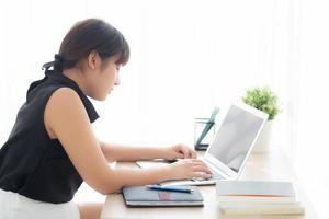 jovem mulher asiática freelance sorrindo trabalhando e digitando no computador portátil no escritório de mesa com profissional, garota usando notebook verificando e-mail ou conceito de rede social, negócios e estilo de vida. foto