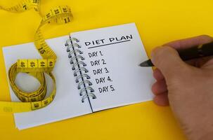 texto de plano de dieta no bloco de notas branco com fita métrica em fundo amarelo. conceito de saúde e dieta foto