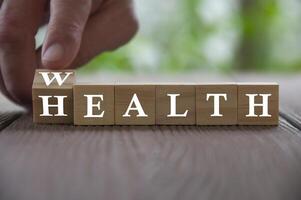 mão flip cubo de madeira com palavra riqueza para a saúde com fundo desfocado da natureza. conceito de riqueza e saúde foto