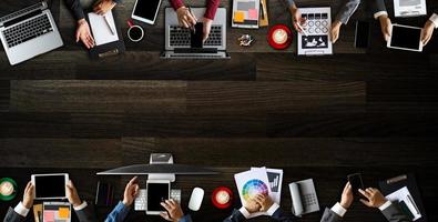 vista superior do grupo de negócios de pessoas ocupadas multiétnicas reunidas com outros no escritório moderno com computador portátil, smartphone, tablet, café e documento na mesa. foto