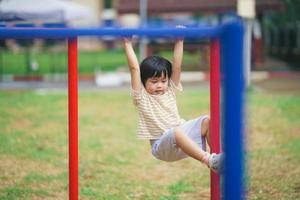 sorriso de linda garota asiática brinca pulando no jardim de infância da escola ou no playground. atividade de verão saudável para crianças. menina asiática escalando ao ar livre no playground. criança brincando no playground. foto