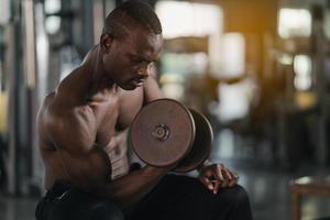 esporte africano homem forte músculo malhando exercício em pesos com haltere na sala de fitness no ginásio. conceito de fitness homem esporte musculação. foto
