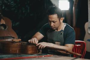 fabricantes de guitarra homem asiático fazendo guitarras acústicas em laboratório. fabricante de guitarra asiático constrói guitarras de alta qualidade para músicos loja de guitarra artesanal. trabalhando bem woodusic, tradição, artesanato antigo. foto