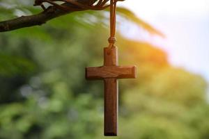 cruz de madeira pendurada no galho de árvore, foco suave e seletivo, fundo de árvore bokeh natural, conceito de esperança, amor, perdão e crença em jesus ao redor do mundo. foto