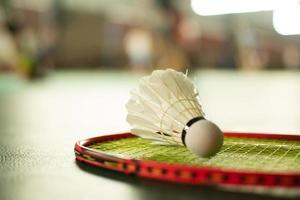 peteca de badminton branca creme e raquete com sombreamento de luz neon no chão verde na quadra de badminton indoor, fundo de badminton desfocado, espaço de cópia. foto