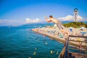 batumi, geórgia, 2022 - turista caucasiano masculino salta para a água do mar do píer batumi no dia quente de verão. férias de férias na costa do mar negro na geórgia. viagem cáucaso foto