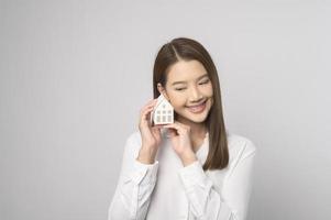 jovem mulher sorridente segurando pequena casa modelo sobre estúdio de fundo branco foto