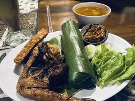 cozinha indonésia ou comida sudanesa chamada nasi timbel, arroz envolto em folhas de bananeira, servido com frango frito, tempeh, tofu, peixe salgado, molho de pimenta, lalap e sayur asem. foto